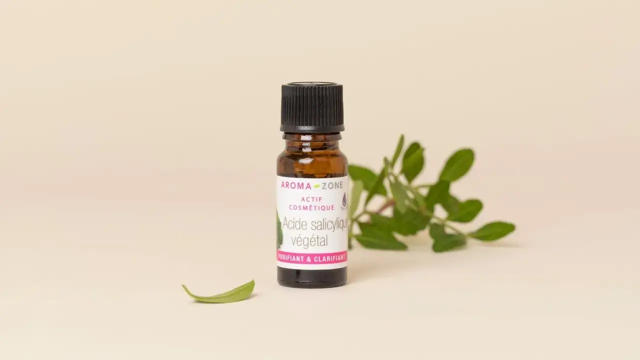 Flacon d'acide salicylique végétal Aroma-Zone, un actif cosmétique purifiant et clarifiant pour la peau, entouré de feuilles vertes.