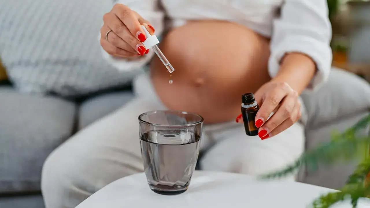 Une femme enceinte ajoute des gouttes d'huile essentielle dans un verre d'eau.