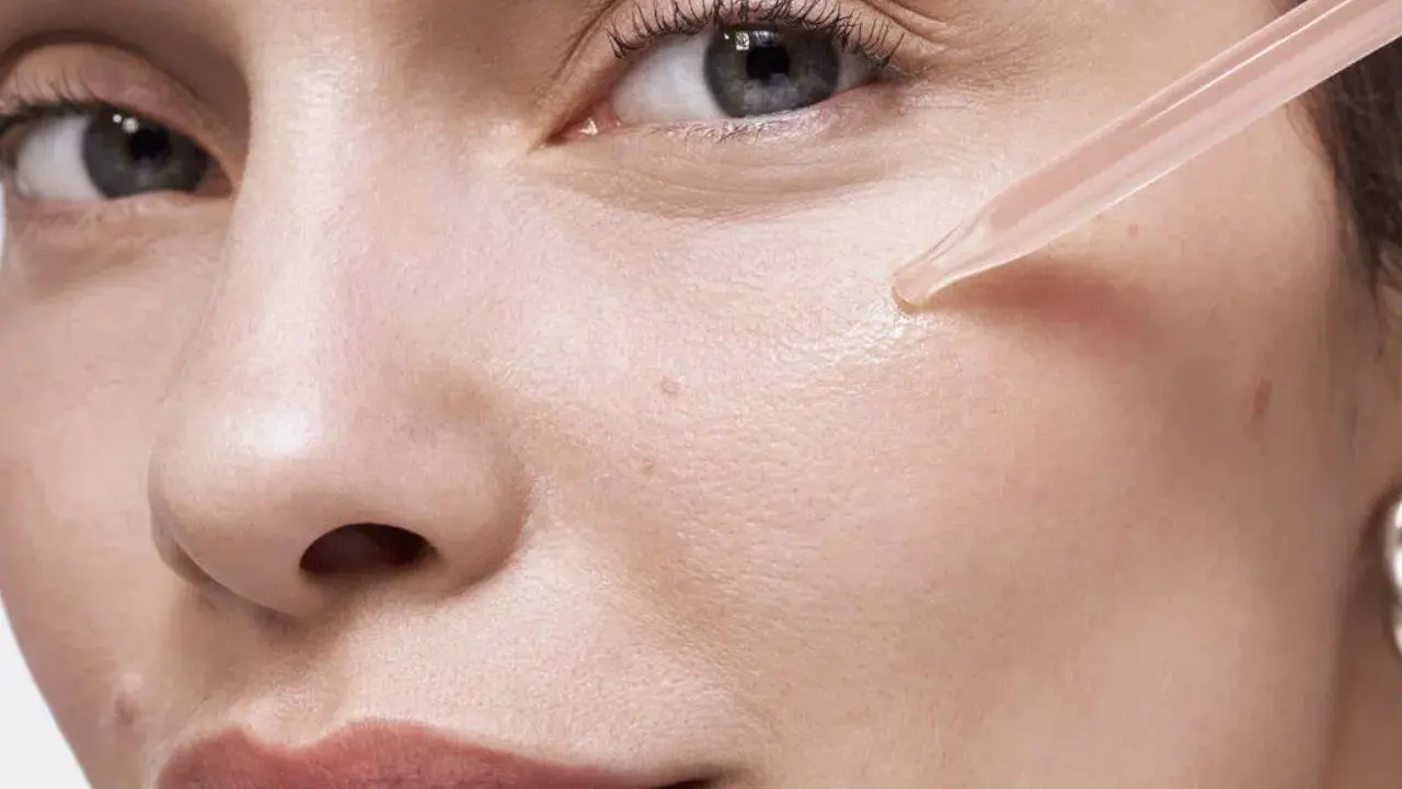 Une pipette dépose une goutte de sérum sur la joue d'une femme. Apprendre comment appliquer un sérum pour une peau éclatante.