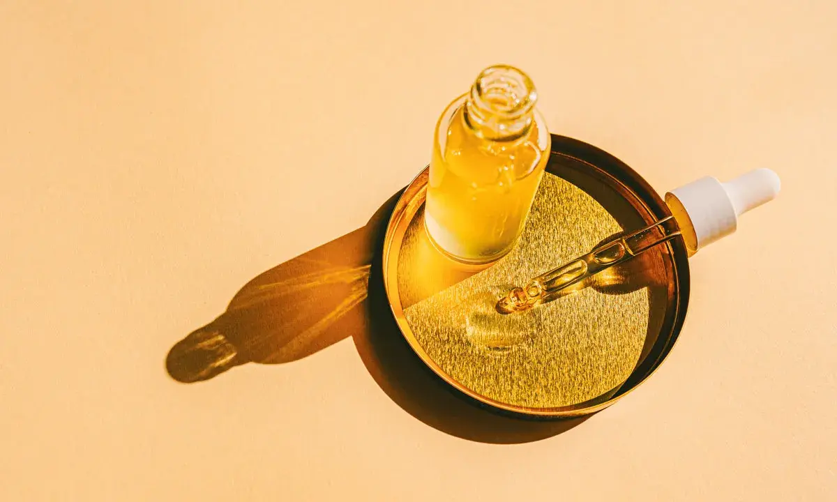 Flacon d'huile de tsubaki doré sur un plateau, avec une pipette prête à délivrer ses bienfaits.