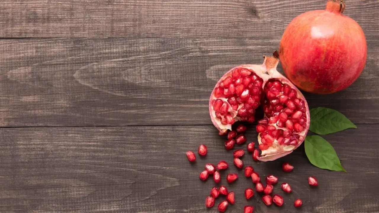 Grenade entière et ouverte, révélant ses arilles rouges. Un fruit aux multiples bienfaits pour la peau, posé sur un fond de bois sombre.