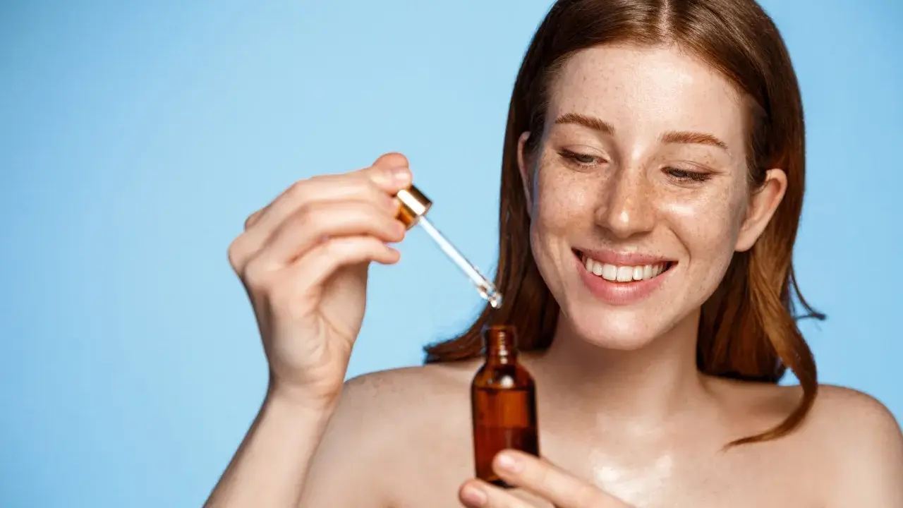 Femme rousse souriante appliquant un sérum. Attention au tocophérol danger potentiel dans certains produits.