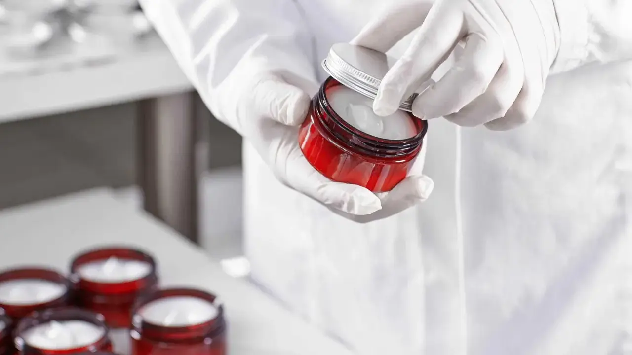 Mains gantées ouvrant un pot de crème cosmétique. Le polysorbate 60 est un ingrédient clé pour sa texture.