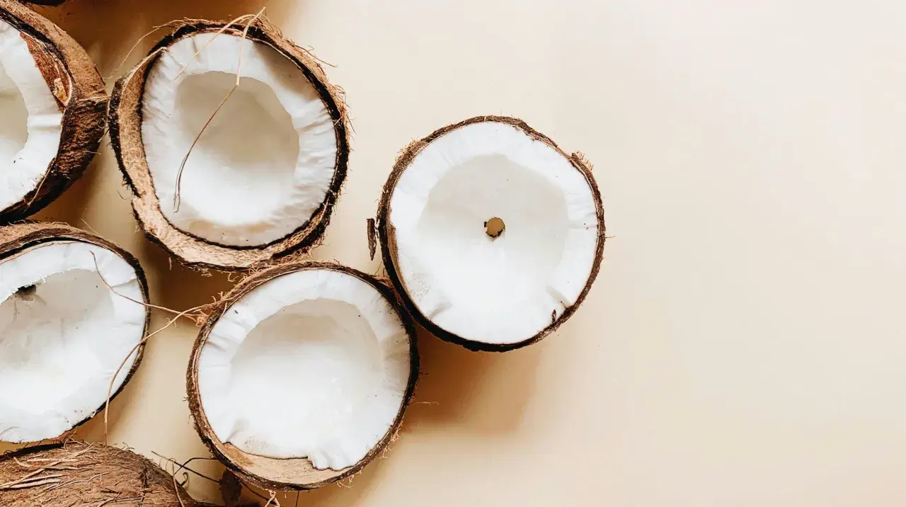 Plusieurs moitiés de noix de coco fraîches sur fond beige. Un aperçu des bienfaits de l'huile de coco.