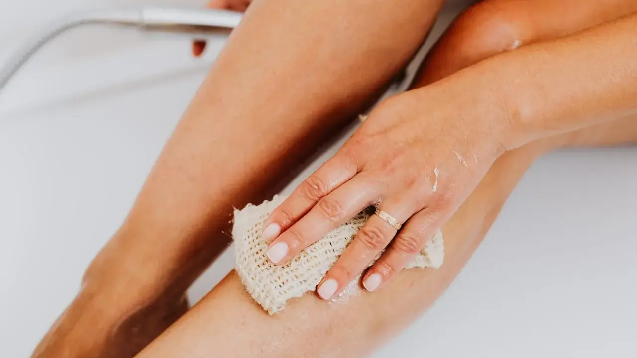 Main d'une femme utilisant une éponge pour exfolier sa peau douce et soyeuse dans la baignoire.