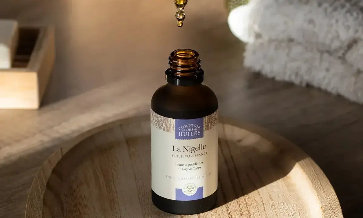 Goutte d'huile de nigelle purifiante tombant dans un flacon, idéale pour l'acné et les peaux à problèmes.