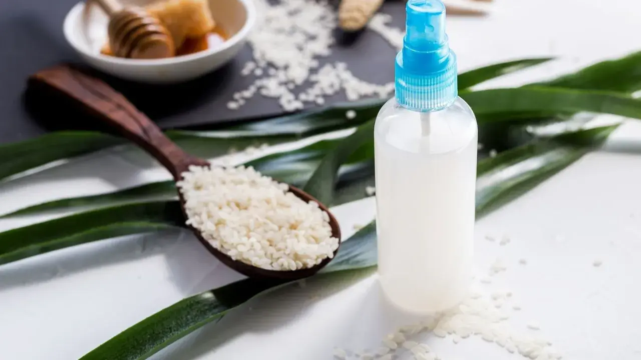 Bouteille de spray contenant de l'eau de riz pour le visage, avec une cuillère de riz et du miel en arrière-plan.