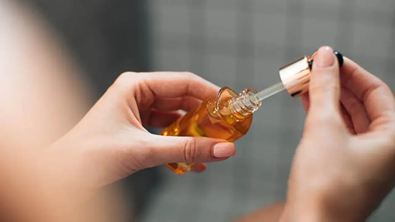 Mains de femme tenant un flacon compte-gouttes d'huile dorée, attention au danger du niacinamide mal utilisé.