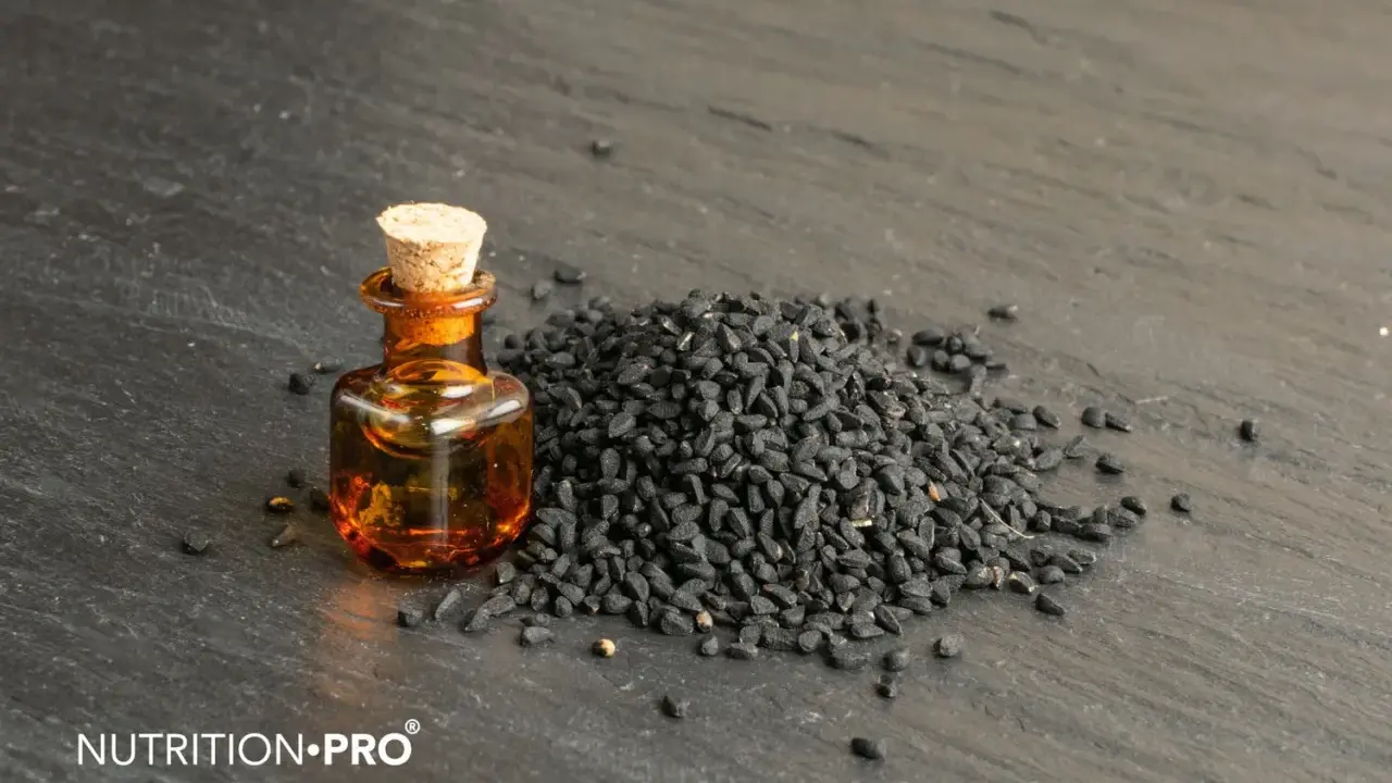 Huile de nigelle dans un flacon, à côté d'une pile de graines noires. Découvrez comment utiliser l'huile de nigelle pour ses bienfaits.