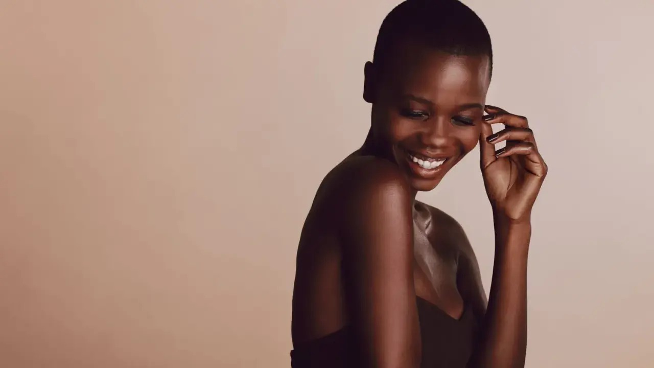 Une femme rit, sa peau foncée, riche en mélanine, le pigment responsable de la couleur de la peau, brille sous la lumière.