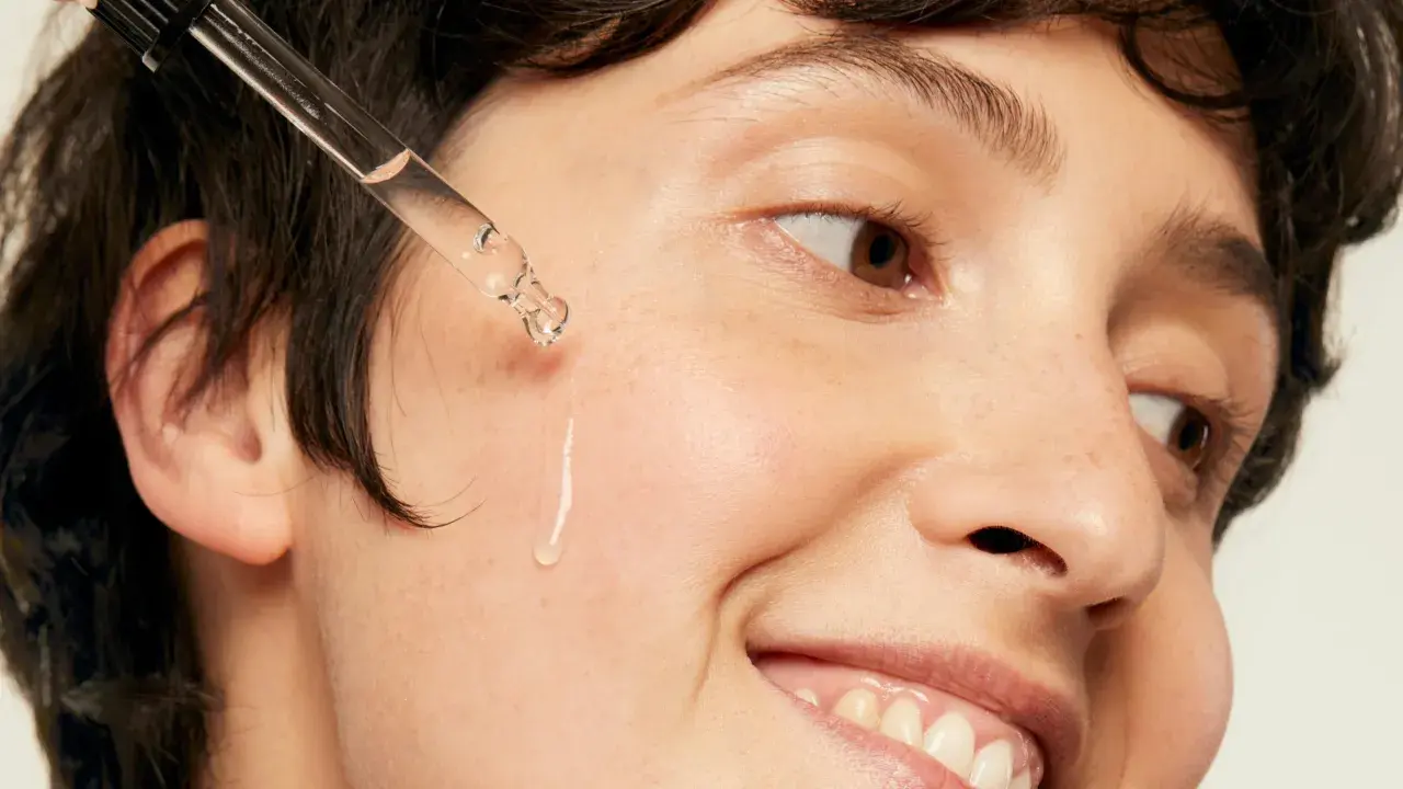 Une goutte d'acide hyaluronique tombe sur la joue d'une personne souriante, une solution pour l'hydratation et la lutte contre l'acné.