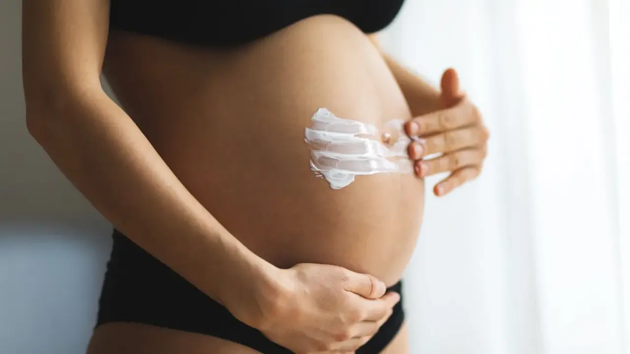 Ventre d'une femme enceinte recevant une crème hydratante. L'acide glycolique est souvent déconseillé pendant la grossesse.