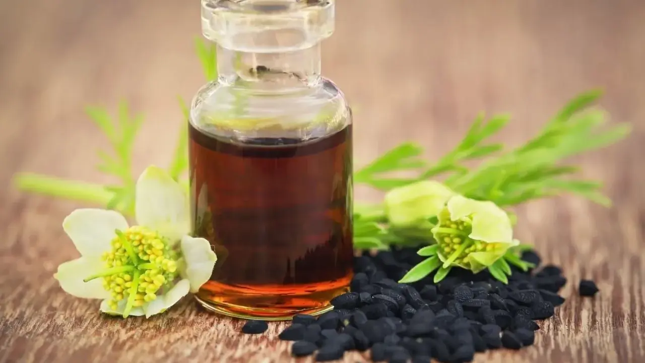 Flacon d'huile de nigelle, graines noires et fleurs sur fond de bois. Attention, l'huile de nigelle peut être dangereuse si mal utilisée.