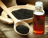 Huile de nigelle : découvrez les bienfaits pour la peau. Des graines noires dans une cuillère en bois et une bouteille d'huile ambrée sur fond rustique.