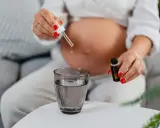 Une femme enceinte ajoute des gouttes d'huile essentielle dans un verre d'eau.