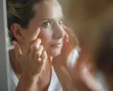 Une femme examine son visage dans un miroir, préoccupée par les signes de glycation, un processus qui affecte la peau.