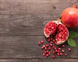 Grenade entière et ouverte, révélant ses arilles rouges. Un fruit aux multiples bienfaits pour la peau, posé sur un fond de bois sombre.