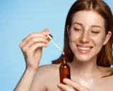 Femme rousse souriante appliquant un sérum. Attention au tocophérol danger potentiel dans certains produits.