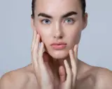 Jeune femme aux yeux bleus, mains sur les joues. Son teint est lumineux, sans aucun teint gris cause.