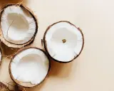 Plusieurs moitiés de noix de coco fraîches sur fond beige. Un aperçu des bienfaits de l'huile de coco.