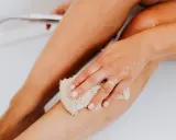 Main d'une femme utilisant une éponge pour exfolier sa peau douce et soyeuse dans la baignoire.