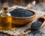 Flacon d'huile de nigelle à côté d'un bol de graines noires. L'huile de nigelle est réputée pour soulager l'eczéma.