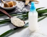 Bouteille de spray contenant de l'eau de riz pour le visage, avec une cuillère de riz et du miel en arrière-plan.