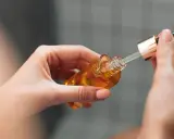 Mains de femme tenant un flacon compte-gouttes d'huile dorée, attention au danger du niacinamide mal utilisé.