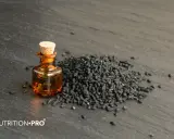 Huile de nigelle dans un flacon, à côté d'une pile de graines noires. Découvrez comment utiliser l'huile de nigelle pour ses bienfaits.