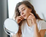 Jeune femme examinant un bouton sur sa joue, se demandant si le dentifrice pourrait aider.