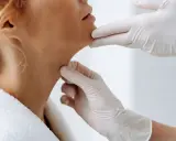 Mains gantées examinant le cou d'une femme, évaluant la peau et le ride du cou.