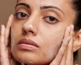 Une femme applique un nettoyant moussant sur son visage, suivant un protocole soin visage. Ses mains massent doucement sa peau.