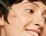Une goutte d'acide hyaluronique tombe sur la joue d'une personne souriante, une solution pour l'hydratation et la lutte contre l'acné.