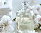 Bouteille de glycérine entourée de fleurs blanches. Attention, la glycérine peut présenter un danger si mal utilisée.