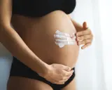 Ventre d'une femme enceinte recevant une crème hydratante. L'acide glycolique est souvent déconseillé pendant la grossesse.
