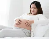 Femme enceinte se grattant le ventre, visiblement gênée par une peau sèche pendant la grossesse.