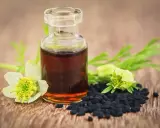 Flacon d'huile de nigelle, graines noires et fleurs sur fond de bois. Attention, l'huile de nigelle peut être dangereuse si mal utilisée.