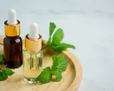 Deux flacons d'huile végétale, entourés de feuilles de menthe fraîche, suggèrent un remède naturel pour le psoriasis.
