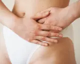 Mains sur le ventre, une femme porte une culotte blanche. Une légère plaque rouge est visible sur son pubis.