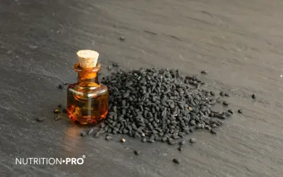 Huile de nigelle dans un flacon, à côté d'une pile de graines noires. Découvrez comment utiliser l'huile de nigelle pour ses bienfaits.