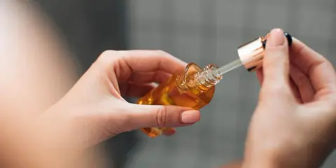 Mains de femme tenant un flacon compte-gouttes d'huile dorée, attention au danger du niacinamide mal utilisé.