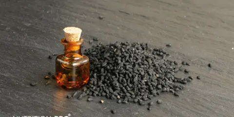 Huile de nigelle dans un flacon, à côté d'une pile de graines noires. Découvrez comment utiliser l'huile de nigelle pour ses bienfaits.