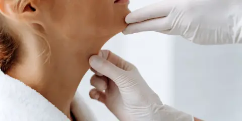 Mains gantées examinant le cou d'une femme, évaluant la peau et le ride du cou.