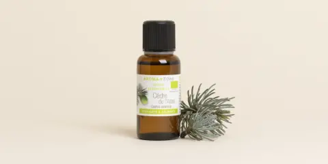 Flacon d'huile essentielle de cèdre de l'Atlas, avec une branche de cèdre. Attention, l'huile essentielle de cèdre peut présenter un danger si mal utilisée.