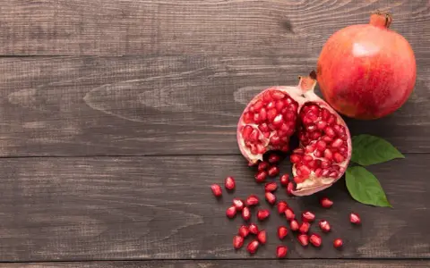 Grenade entière et ouverte, révélant ses arilles rouges. Un fruit aux multiples bienfaits pour la peau, posé sur un fond de bois sombre.