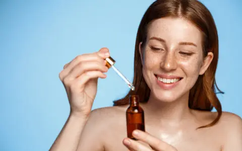 Femme rousse souriante appliquant un sérum. Attention au tocophérol danger potentiel dans certains produits.