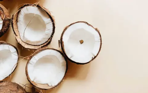Plusieurs moitiés de noix de coco fraîches sur fond beige. Un aperçu des bienfaits de l'huile de coco.