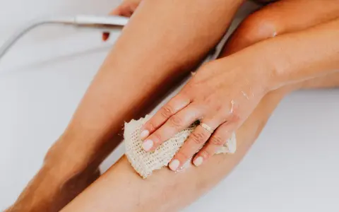 Main d'une femme utilisant une éponge pour exfolier sa peau douce et soyeuse dans la baignoire.