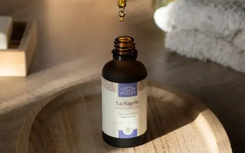 Goutte d'huile de nigelle purifiante tombant dans un flacon, idéale pour l'acné et les peaux à problèmes.
