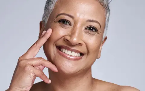 Portrait d'une femme souriante, sa peau qui marque les plis témoigne d'une vie riche. Ses doigts effleurent délicatement sa joue.